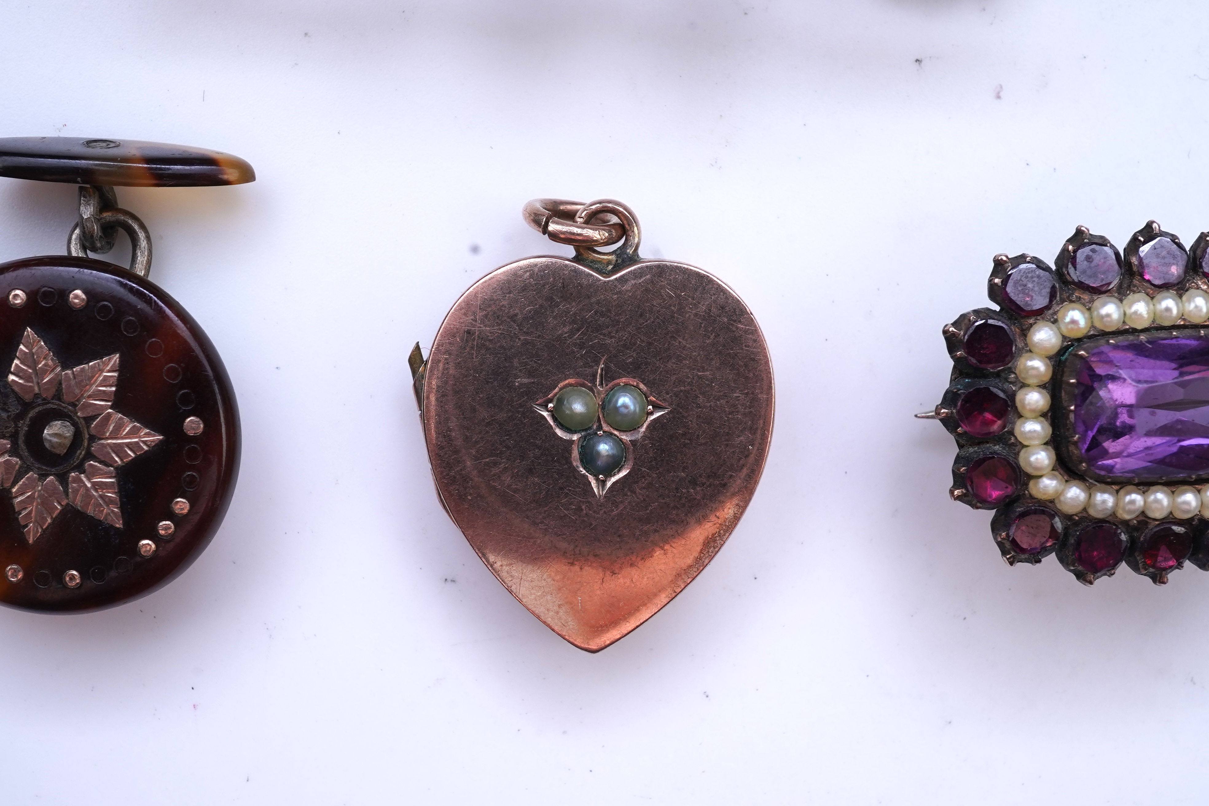 A Victorian yellow metal, amethyst and garnet cluster set brooch, 22mm, an early 20th century yellow metal and seed pearl set heart shaped locket, a yellow metal, garnet and zircon set three stone bar brooch and a tortoi